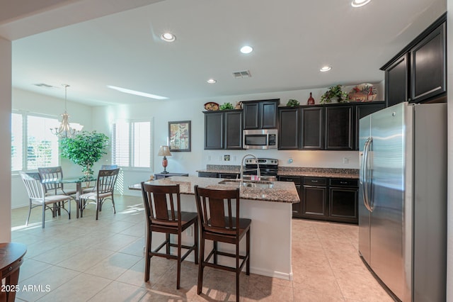 kitchen featuring light stone countertops, pendant lighting, appliances with stainless steel finishes, sink, and a center island with sink