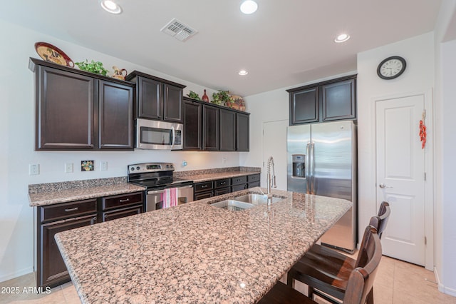 kitchen with appliances with stainless steel finishes, an island with sink, sink, a breakfast bar, and light tile patterned floors