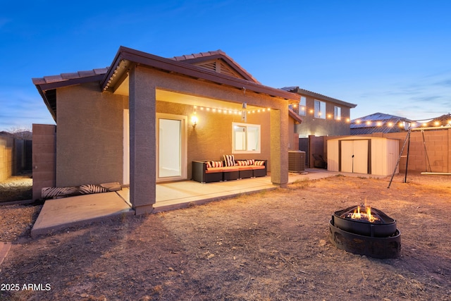 back house at dusk with central AC, a shed, an outdoor living space with a fire pit, and a patio area