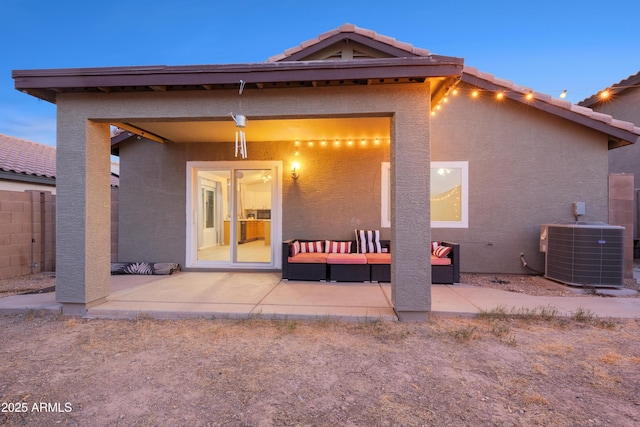 back house at dusk with outdoor lounge area, a patio, and central air condition unit