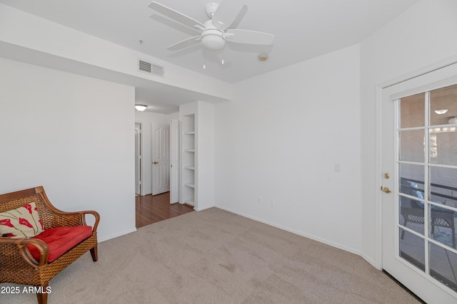 living area with ceiling fan, built in shelves, and light colored carpet