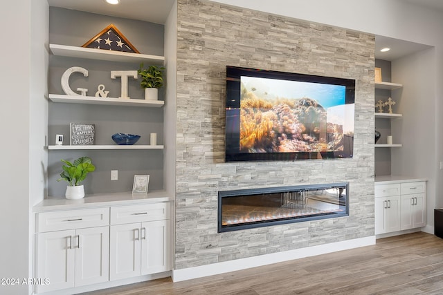 interior details with wood-type flooring, a stone fireplace, and built in shelves