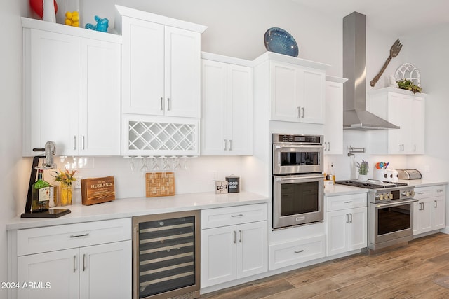 kitchen with stainless steel appliances, light hardwood / wood-style flooring, beverage cooler, and wall chimney exhaust hood