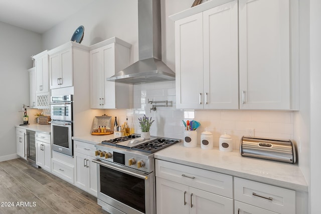 kitchen with appliances with stainless steel finishes, light hardwood / wood-style flooring, white cabinetry, and wall chimney range hood