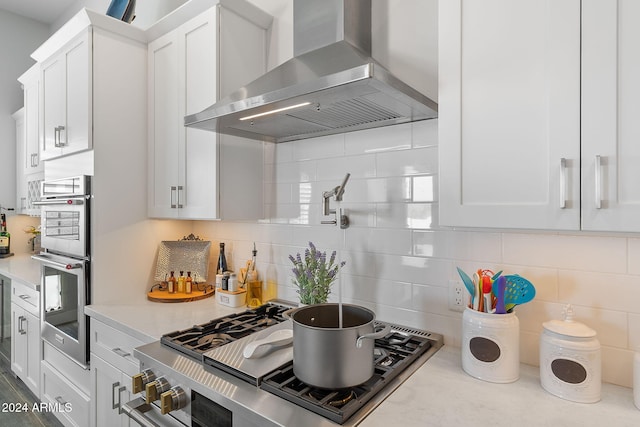 kitchen featuring light stone countertops, wall chimney exhaust hood, decorative backsplash, white cabinets, and appliances with stainless steel finishes