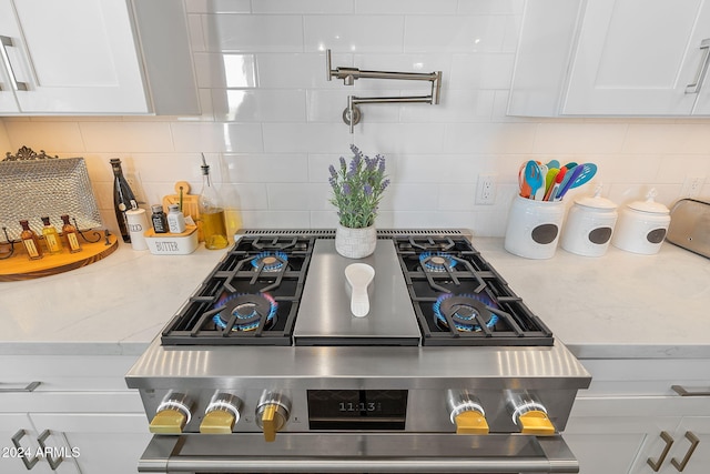 kitchen featuring decorative backsplash, light stone counters, white cabinetry, and stainless steel stove