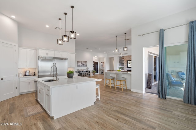 kitchen with stainless steel appliances, light hardwood / wood-style flooring, white cabinetry, hanging light fixtures, and an island with sink