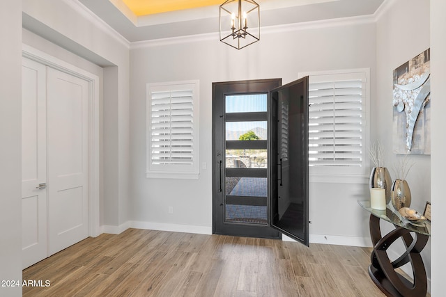 foyer with crown molding, a notable chandelier, and light wood-type flooring