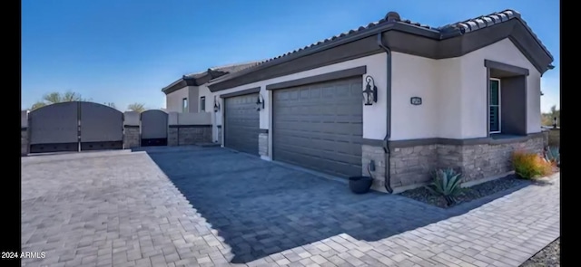 8523 N 192nd Ave, Waddell, AZ 85355 - view of side of property featuring an attached garage, decorative driveway, stone siding, a gate, and stucco siding
