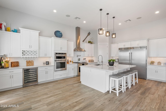 kitchen featuring premium appliances, sink, wall chimney range hood, white cabinets, and wine cooler