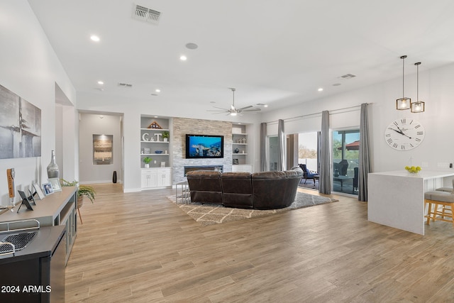 living room with built in shelves, ceiling fan, a fireplace, and light wood-type flooring