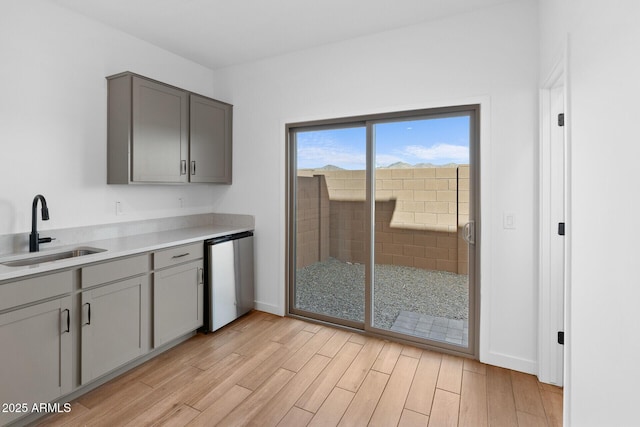 kitchen featuring sink, gray cabinets, dishwasher, and light wood-type flooring