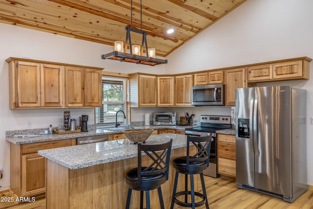 kitchen with sink, a center island, appliances with stainless steel finishes, pendant lighting, and light stone countertops