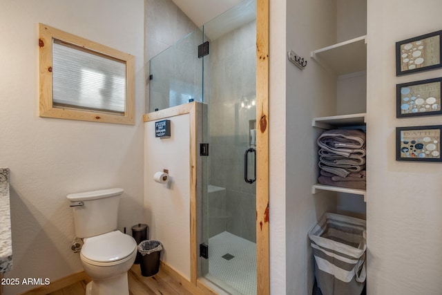 bathroom with wood-type flooring, a shower with shower door, and toilet