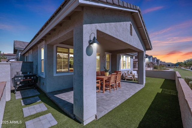 patio terrace at dusk featuring area for grilling and a lawn