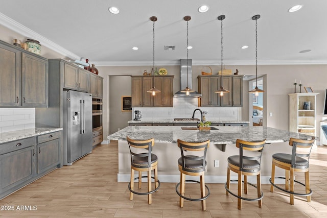 kitchen with pendant lighting, stainless steel appliances, a large island, and wall chimney range hood