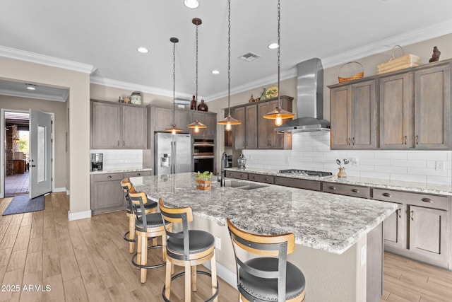 kitchen with hanging light fixtures, appliances with stainless steel finishes, a center island with sink, and wall chimney exhaust hood