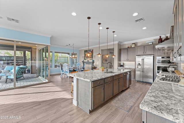 kitchen featuring a spacious island, sink, decorative light fixtures, stainless steel appliances, and light stone countertops