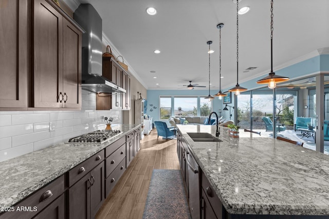 kitchen with pendant lighting, a large island, stainless steel appliances, light stone countertops, and wall chimney exhaust hood