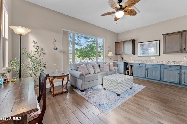 living room featuring ceiling fan, bar area, and light wood-type flooring