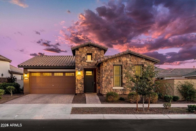 view of front facade with an attached garage, a tile roof, stone siding, decorative driveway, and stucco siding