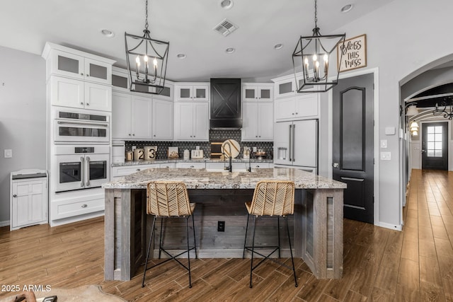 kitchen featuring arched walkways, a chandelier, white appliances, visible vents, and backsplash