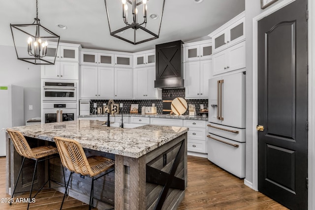 kitchen with a notable chandelier, dark wood-type flooring, a sink, white appliances, and premium range hood