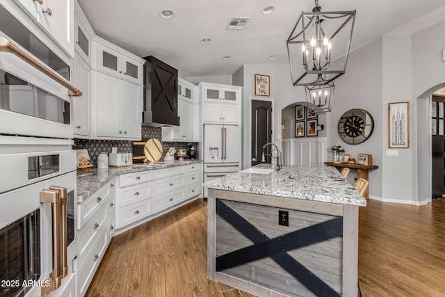 kitchen with arched walkways, white appliances, wood finished floors, a sink, and backsplash