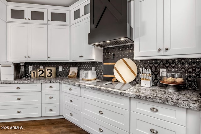 kitchen featuring dark wood-style flooring, black electric stovetop, tasteful backsplash, white cabinets, and premium range hood