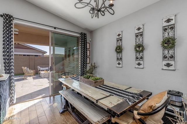 dining area with an inviting chandelier, vaulted ceiling, and wood finished floors