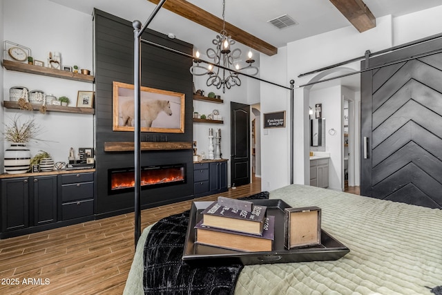 bedroom featuring a barn door, a large fireplace, visible vents, light wood finished floors, and beamed ceiling