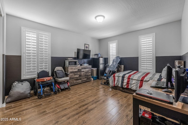 bedroom with freestanding refrigerator, a textured ceiling, and wood finished floors