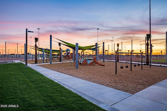 playground at dusk featuring fence, playground community, and a yard