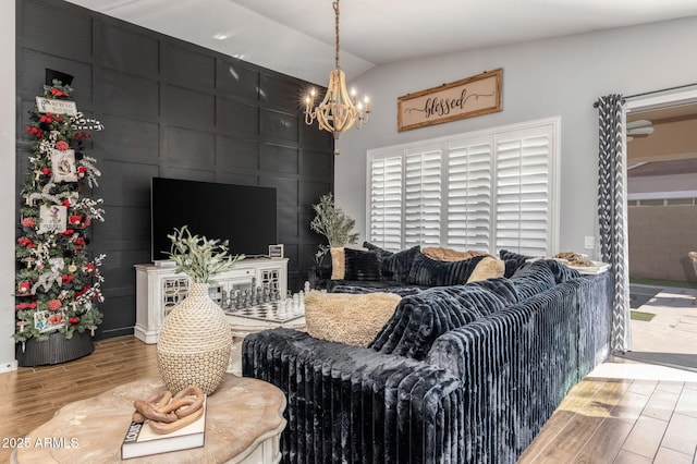 living area featuring a notable chandelier, vaulted ceiling, a decorative wall, and wood finished floors