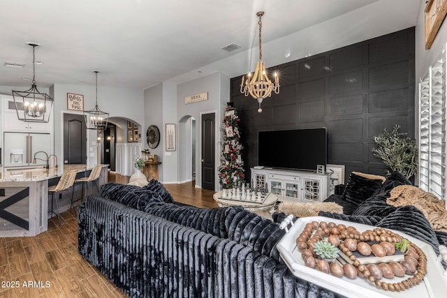 living room featuring arched walkways, visible vents, light wood-style flooring, and an inviting chandelier