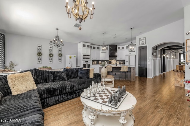 living area with arched walkways, visible vents, light wood-style flooring, and an inviting chandelier