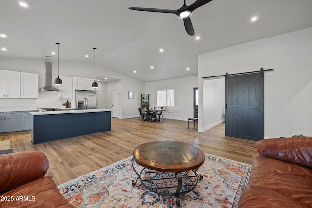 living room featuring vaulted ceiling, ceiling fan, a barn door, and light wood-type flooring