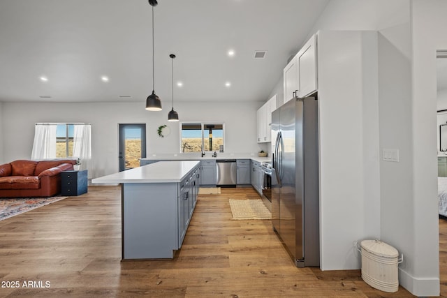 kitchen featuring a kitchen island, white cabinetry, hanging light fixtures, light hardwood / wood-style floors, and stainless steel appliances