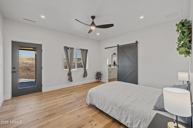 bedroom with ceiling fan, a barn door, and light hardwood / wood-style flooring