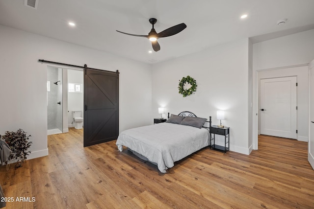 bedroom featuring ceiling fan, a barn door, connected bathroom, and light hardwood / wood-style floors