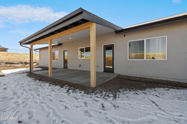 snow covered rear of property featuring a patio area