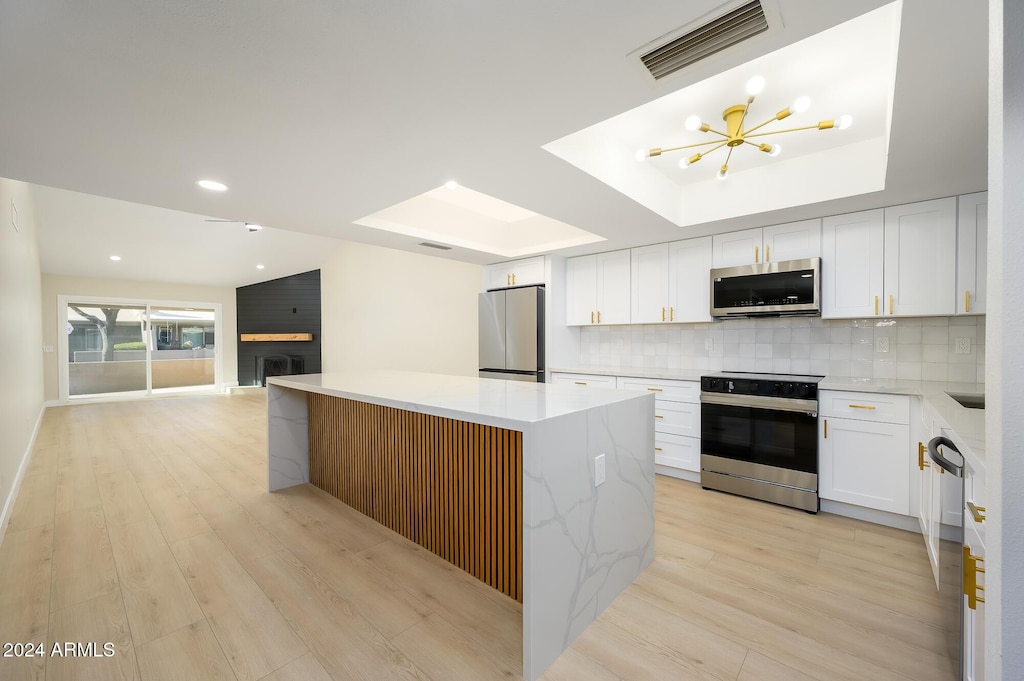 kitchen with a center island, white cabinetry, stainless steel appliances, a raised ceiling, and a brick fireplace