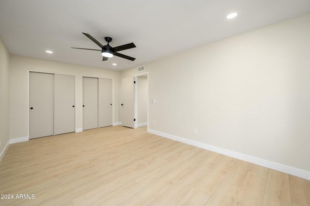 unfurnished bedroom featuring ceiling fan, light hardwood / wood-style floors, and two closets