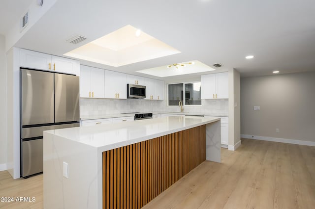 kitchen featuring sink, white cabinets, a tray ceiling, a kitchen island, and stainless steel appliances