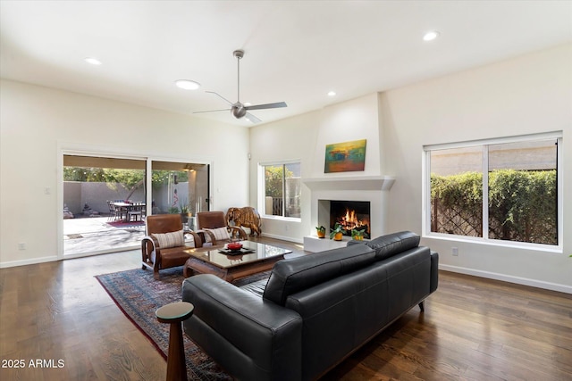 living room featuring dark wood-type flooring, ceiling fan, and a large fireplace