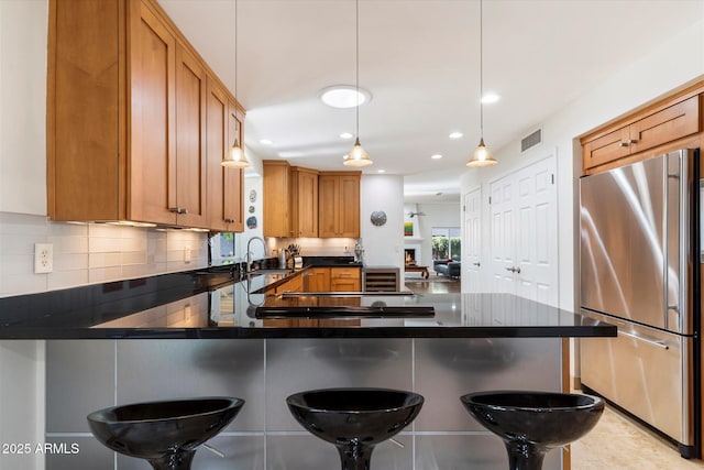 kitchen with decorative light fixtures, kitchen peninsula, a breakfast bar, and stainless steel refrigerator