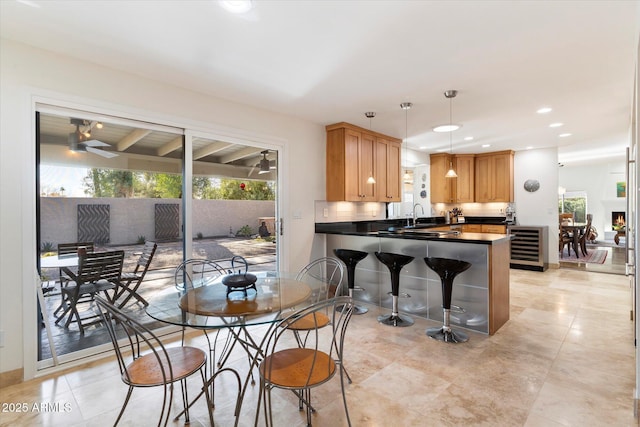 kitchen with kitchen peninsula, decorative backsplash, beverage cooler, pendant lighting, and sink