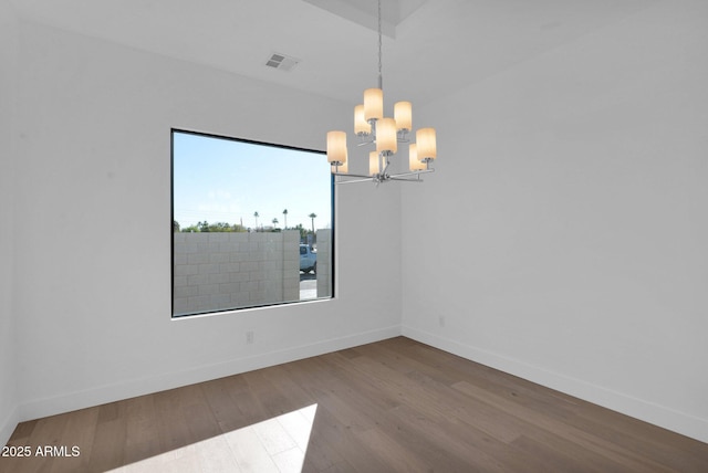 spare room with hardwood / wood-style floors and an inviting chandelier