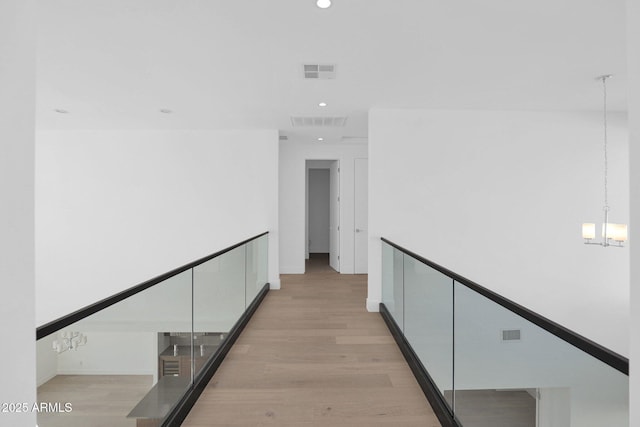 hallway with light wood-type flooring and a chandelier