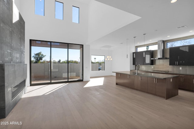 kitchen featuring sink, wall chimney exhaust hood, gas stovetop, dark brown cabinetry, and pendant lighting